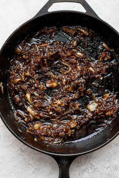 an iron skillet filled with food on top of a white countertop next to a wooden spoon