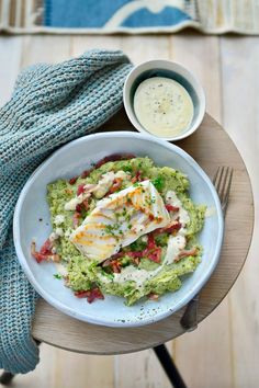 a white plate topped with broccoli covered in chicken next to a bowl of ranch dressing