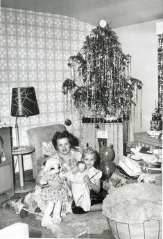 an old black and white photo of a woman sitting with her child in front of a christmas tree