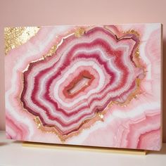 a pink and gold painting on a white shelf