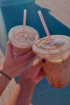 two people holding up drinks with straws in their hands on the edge of a swimming pool