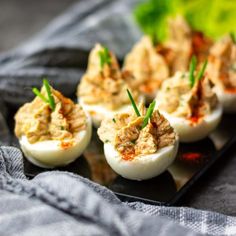 deviled eggs are stuffed with meat and garnished with chives on a black plate