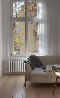 a couch sitting in front of a window next to a table with a laptop on it