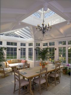 a room filled with lots of windows next to a white table and chairs under a chandelier