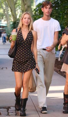 a man and woman walking down the street holding cups in their hands while wearing cowboy boots