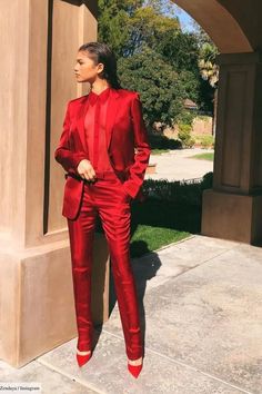 a woman in a red suit standing next to a pillar