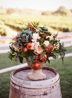 a vase filled with flowers and fruit sitting on top of a barrel