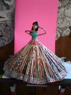 a woman in a dress made out of magazines on top of a table with a pink background