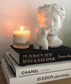 two books stacked on top of each other with a candle next to them and a statue of a child holding a teddy bear