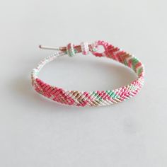 a close up of a bracelet on a white surface with pink, green and red beads