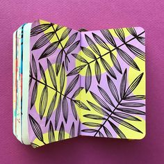 an open notebook with black and yellow leaves on it, against a purple background that matches the color of the paper