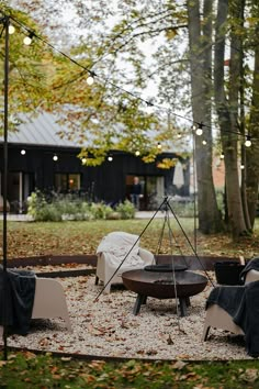 an outdoor fire pit surrounded by chairs and umbrellas in the fall leaves with lights strung overhead