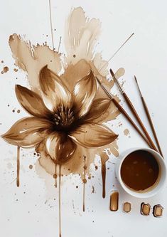 a coffee cup and some brown paint on a white surface with an artistic flower painted on it