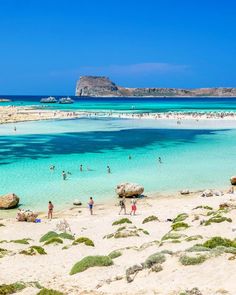 many people are on the beach and in the water near some rocks, sand and seaweed