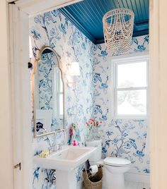 a bathroom with blue and white wallpaper has a basket on the floor next to the toilet