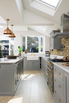 a kitchen with grey cabinets and white counter tops, gold pulls on the handles in front of an open window