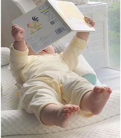 a baby laying on its back with a book in it's hand