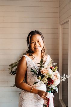 a woman standing in front of a white wall holding a bouquet of flowers and smiling