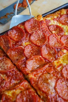 a pepperoni pizza sitting on top of a wooden table next to a spatula