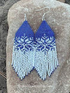 a pair of blue and white beaded earrings sitting on top of a rock