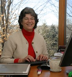 a woman sitting at a desk in front of a laptop computer with a cup of coffee next to her