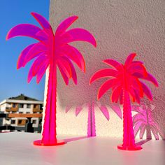 two pink palm trees sitting next to each other on a white counter top in front of a building