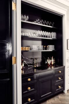 a black and white kitchen with lots of wine glasses on the counter top, gold trimming