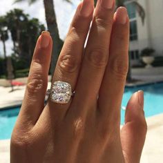 a woman's hand with a diamond ring on her finger next to a swimming pool