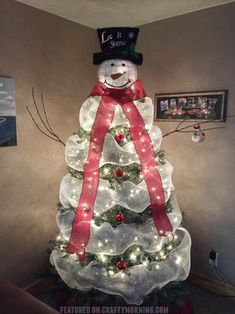 a lighted christmas tree with a snowman top hat and red ribbon on it's head