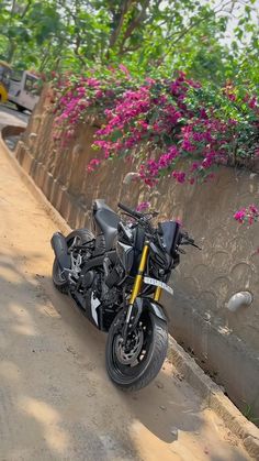 a black motorcycle parked next to a stone wall with flowers growing on the walls behind it