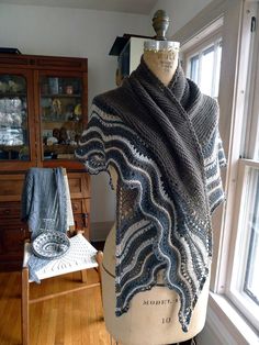 a knitted shawl sits on a mannequin in front of a window