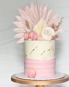 a pink and white cake decorated with flowers on a gold plated stand against a white backdrop