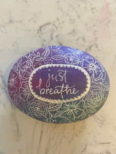 a painted rock with the words just breathe on it sitting on a marble countertop