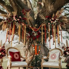 an outdoor ceremony setup with chairs and flowers hanging from the tree trunk, decorated with feathers