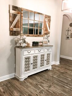 a white dresser with mirrors and vases on top of it in a living room