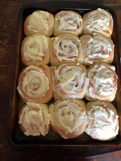 a pan filled with rolls covered in white icing on top of a wooden table