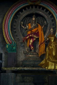 the statue is sitting in front of an ornate wall decoration with gold and red colors