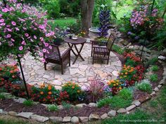 an outdoor patio with chairs and tables surrounded by flowers in the garden, next to a tree