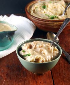 two bowls filled with mashed potatoes sitting on top of a wooden table next to spoons