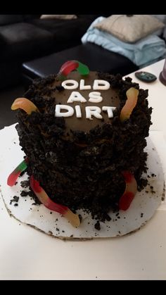 a cake with dirt on it that says old as dirt in white letters and gummy worms around the edges