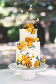 a wedding cake decorated with oranges and yellow flowers on a white tablecloth in front of trees