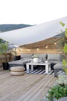 an outdoor living area with couches, tables and plants on the deck under a white awning