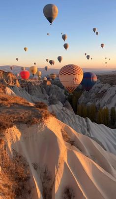 many hot air balloons are flying in the sky over sand dunes and trees at sunset