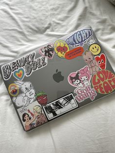 an apple laptop covered in stickers on a bed