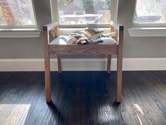 a cat sleeping on top of a wooden chair in front of a window with wood flooring