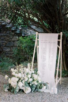 an outdoor ceremony setup with flowers on the ground and a white sign in front of it