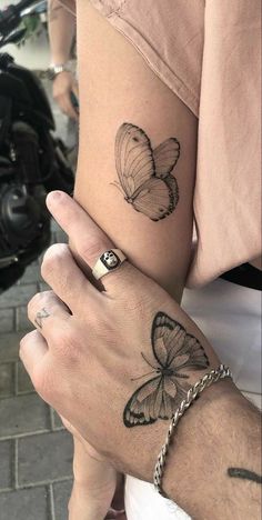 two butterflies tattoo on the arm and wrist, one with a chain around it's ankles