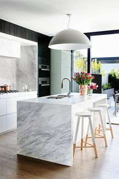 a kitchen with marble counter tops and stools in front of an island that has flowers on it