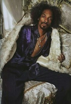 a man with long hair sitting on top of a bed next to a white blanket