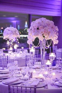 the tables are set with candles and centerpieces for an elegant wedding reception in purple lighting